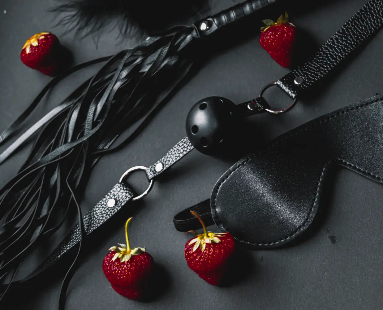 Black leather collar and pet play accessories arranged with strawberries